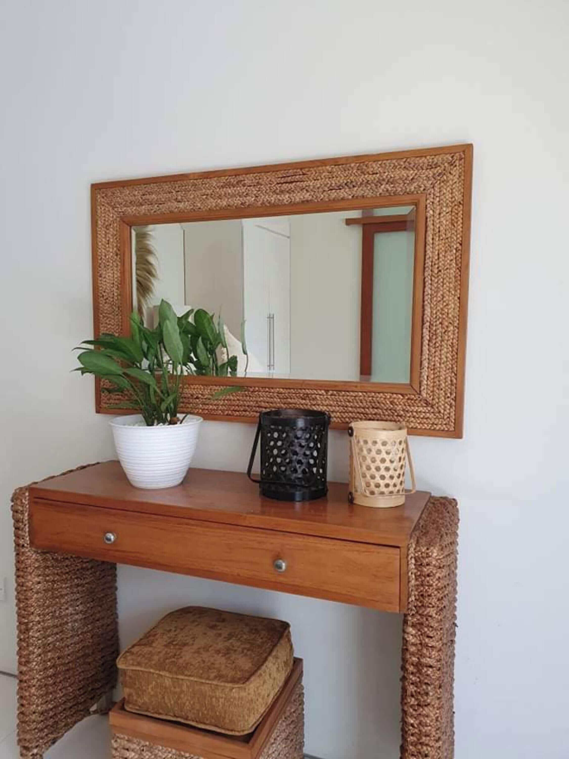 A wooden console table with a woven basket, a potted plant, a black candle holder, and a woven stool.