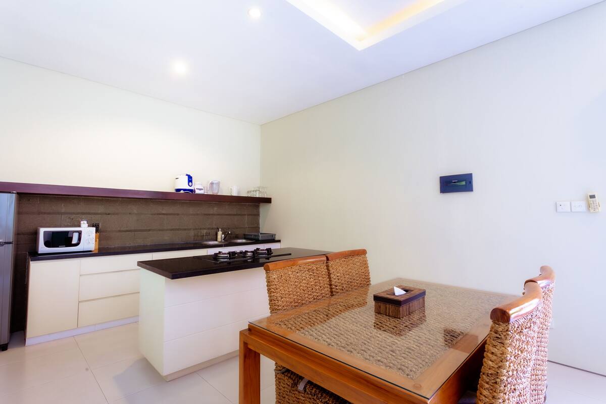 A modern kitchen with a central island, white cabinetry, and a wooden dining table with a woven chair.