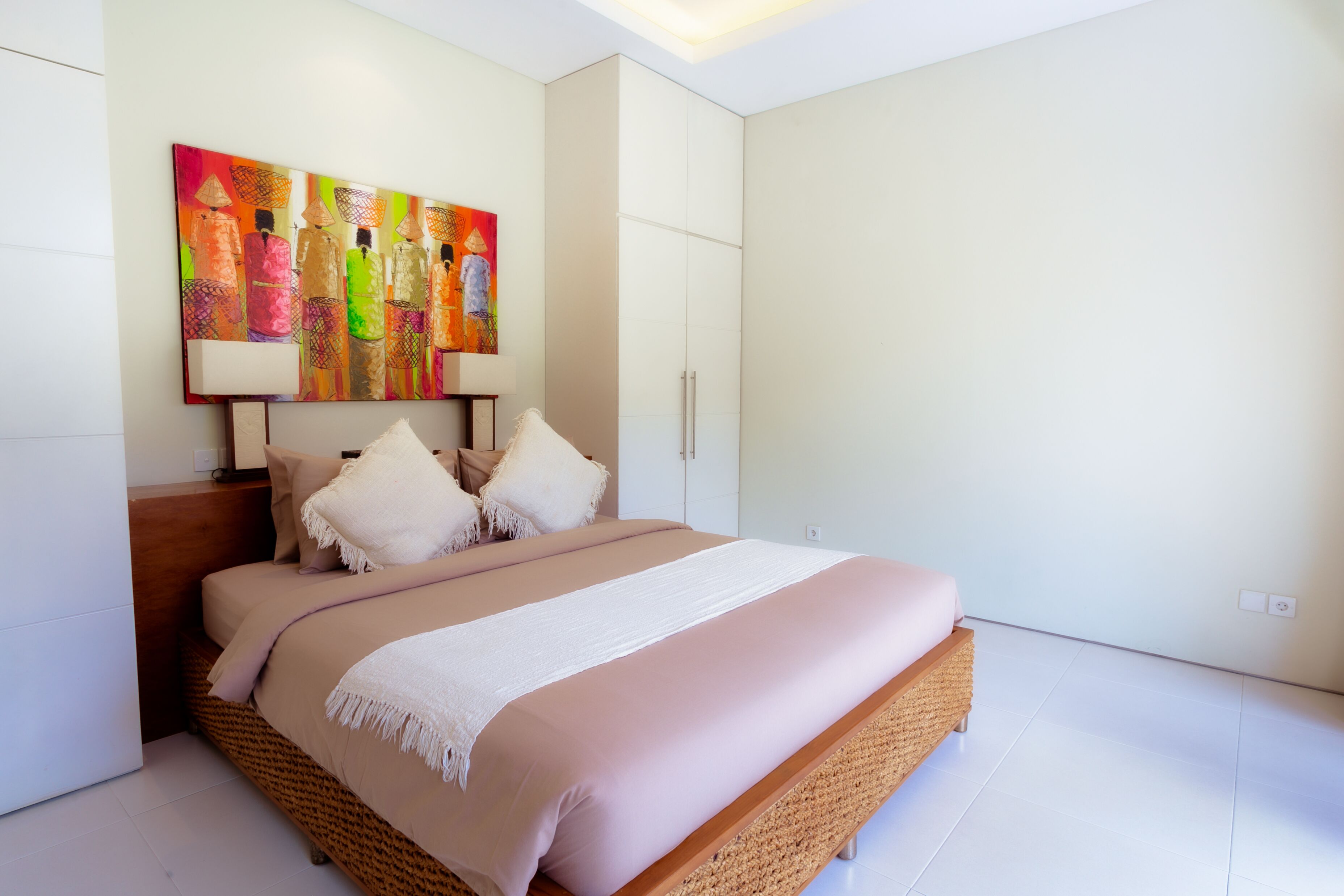 A modern bedroom with a large bed, a headboard with a colorful artwork, and a bedside table with a lamp.