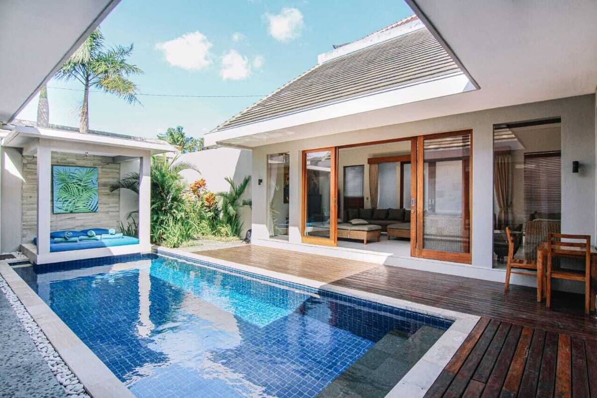 A modern house with a swimming pool, wooden deck, and a patio area.