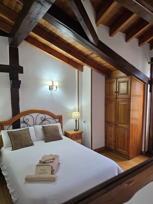 A bedroom with a wooden bed, a nightstand with a lamp, a wardrobe, and a cross beam structure. - Hotel Rural La Posada El Sestil (Vega de Liebana)
