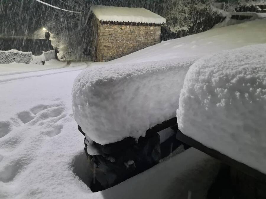 Un vehículo cubierto de nieve estacionado en una zona nevada, con un edificio de piedra al fondo.