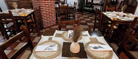 Un restaurante con mesas de madera dispuestas para comer, con individuales tejidos y un jarrón central.
