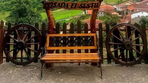 Eine hölzerne Bank vor einer malerischen Berglandschaft, mit einem Schild, auf dem "POSADA EL SESTIL" steht.