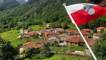 A village with traditional red-tiled roofs, surrounded by lush green hills and mountains.