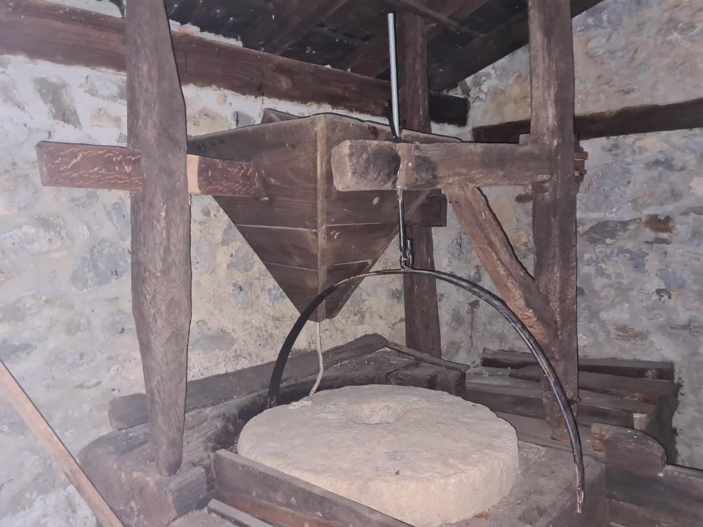 Een stenen molen met houten frame en een trechtervormige constructie.