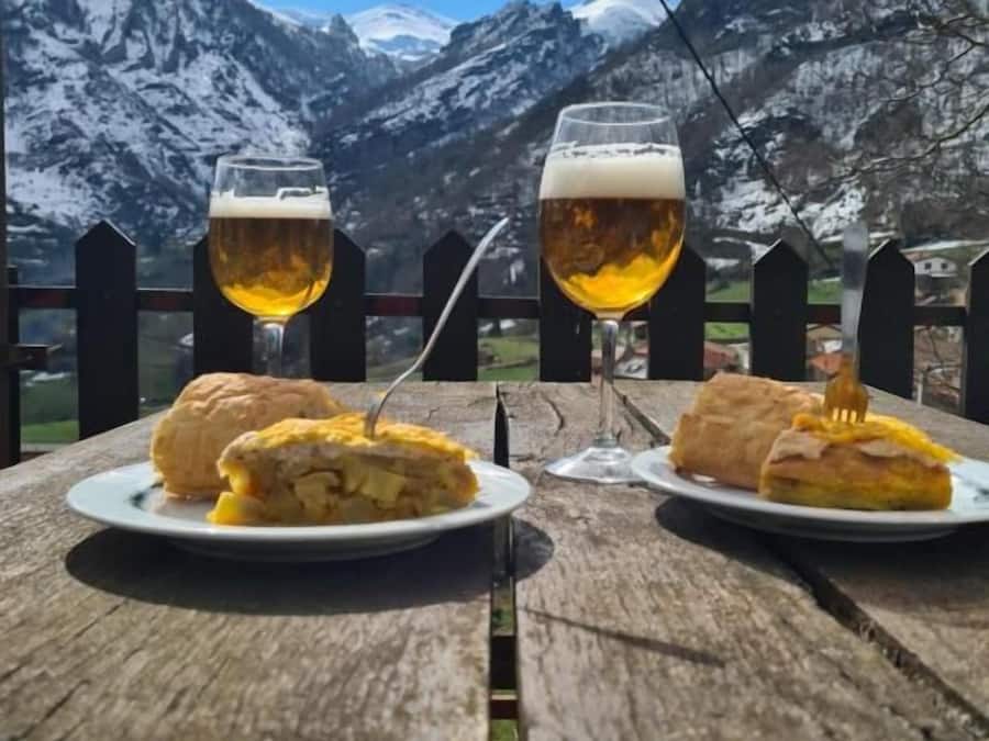 To ølglas på et træbord med sandwiches, med et bjerglandskab i baggrunden.