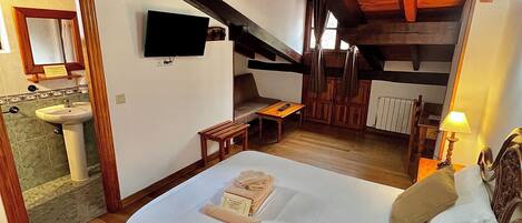 A bedroom with a wooden ceiling, a bed with pillows, a bedside table with a lamp, and a TV mounted on the wall.