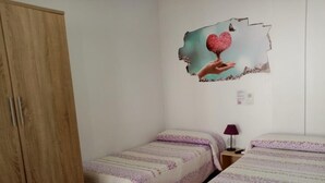 A bedroom with two single beds, a wooden wardrobe, and a wall decoration of a hand holding a heart. - Hostal La Campa (Chiclana de la Frontera)