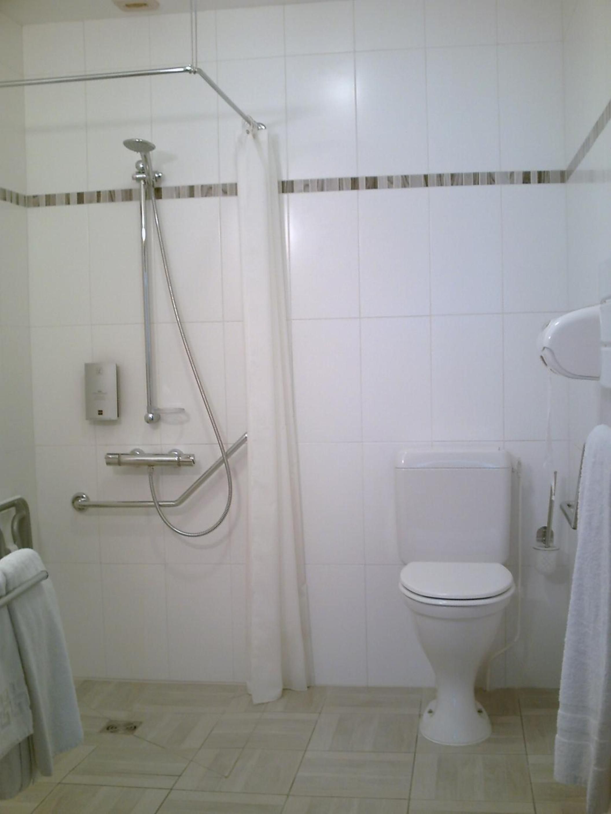 Un baño con ducha, inodoro y barras de apoyo.