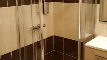 A corner shower enclosure with a glass door, a toilet, and a vanity with drawers.