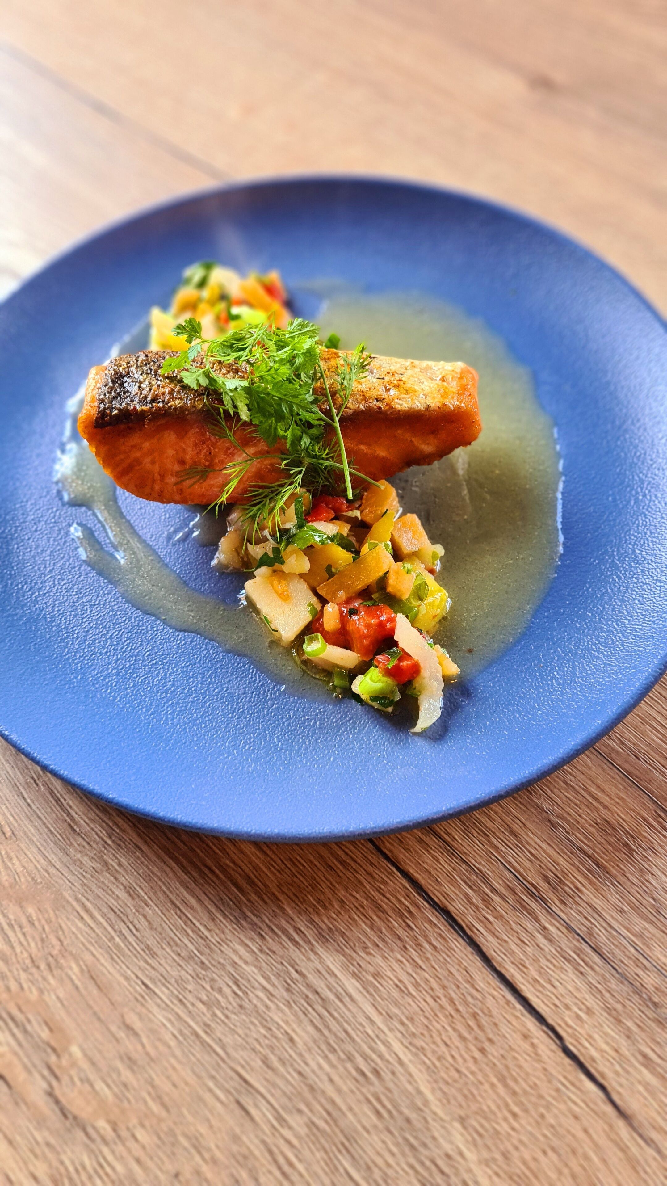 Ein blauer Teller mit Lachs und gemischtem Gemüse.