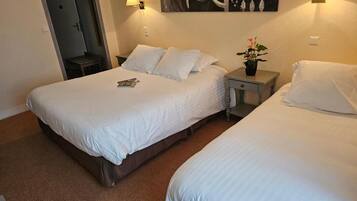 A hotel room with two beds, a door, a wall-mounted artwork, and a nightstand with a lamp.