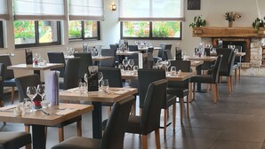 Een restaurant met houten tafels en stoelen, grote ramen met uitzicht en hangende lampen.