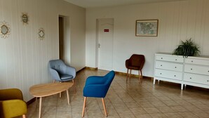 Een hotel lobby met een houten tafel, twee fauteuils, een bruine stoel, een witte dressoir en een kaart aan de muur.