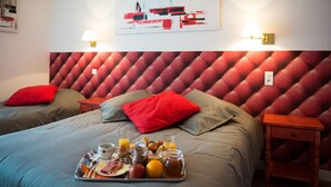 Een hotelkamer met twee bedden, een rode hoofdbord, een ontbijtplateau op het bed en een aan de muur hangend kunstwerk.