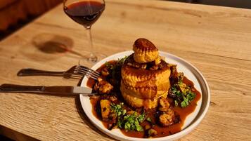 Un plato de comida con una copa de vino tinto sobre una mesa de madera.