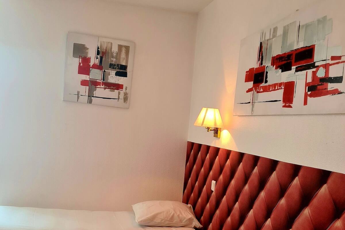 Een hotelkamer met twee bedden, een rood beklede hoofdeinde en kunst aan de muur.