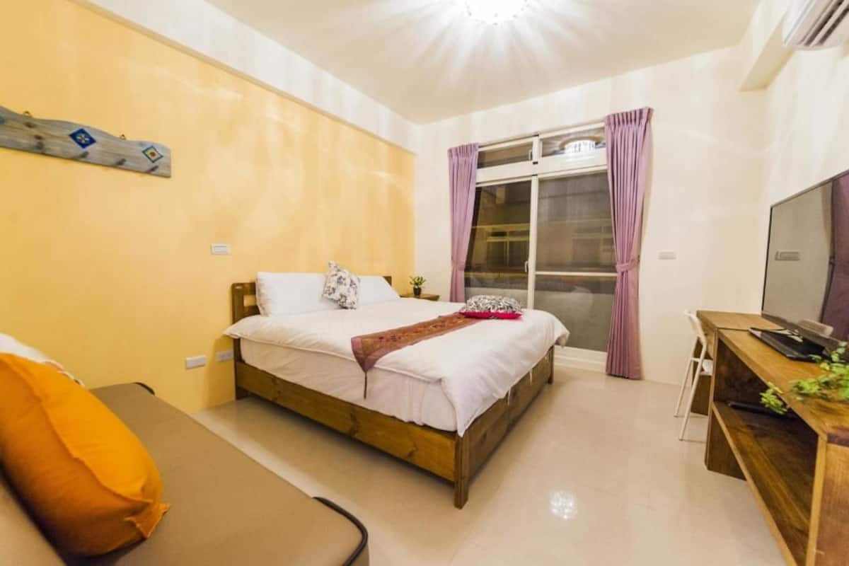 A bedroom with a bed, a desk, a chair, and a TV.