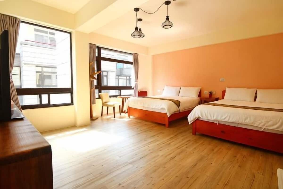 A hotel room with two beds, a desk, a chair, and a large window.