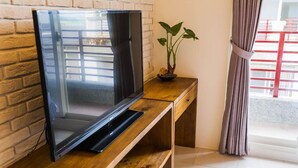 A modern living room with a flat-screen TV on a wooden console table, a potted plant, and a view of a balcony with a red railing. - Happy Snails (Wujie)