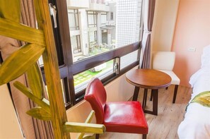 Habitación de hotel con cama, una mesita, una silla roja y ventana con vistas al exterior.