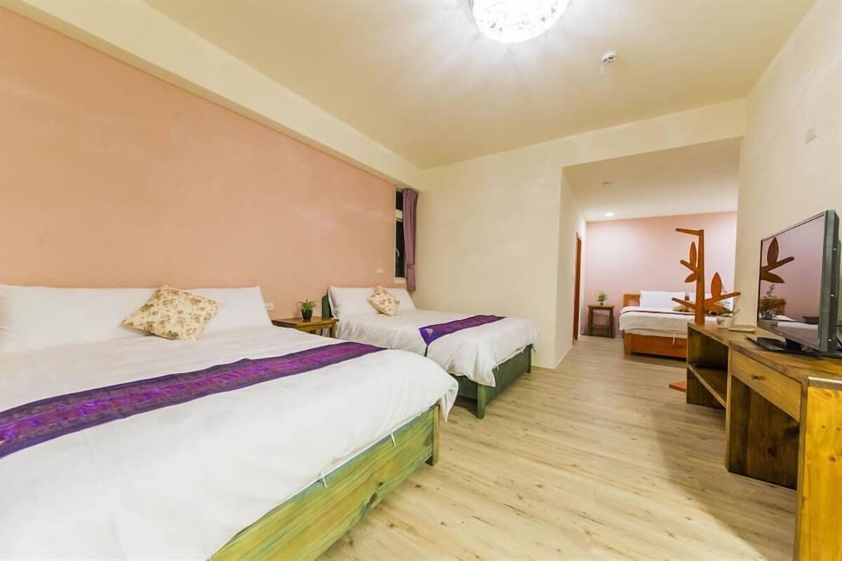 A hotel room with two single beds, wooden flooring, a TV, and a desk.