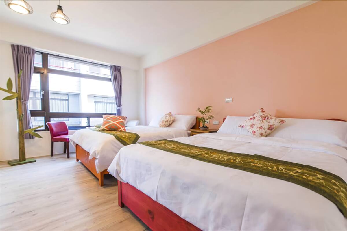 A hotel room with two beds, a red chair, a window with curtains, and a plant.