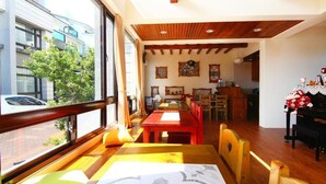 A dining area with wooden furniture, a piano, and a view of the street. - Happy Snails (Wujie)