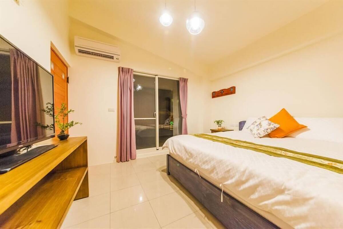A modern hotel room with a large bed, a wooden desk, and a sliding glass door leading to a balcony.