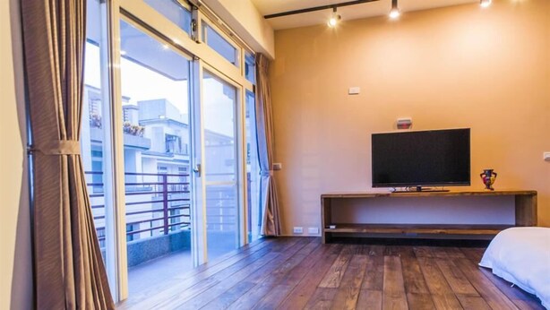 A hotel room with a large sliding glass door leading to a balcony, a flat-screen TV on a wooden stand, and a bed with white bedding. - Happy Snails (Wujie)