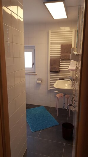 A bathroom with white tiles, a window, a towel rack, a sink, and a blue mat.