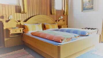 Una cama de madera con una colcha y almohadas de colores, una mesita de noche con una lámpara y una ventana con cortinas.