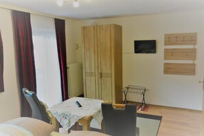 A room with a dining table, chairs, a wardrobe, a TV, and a drying rack.