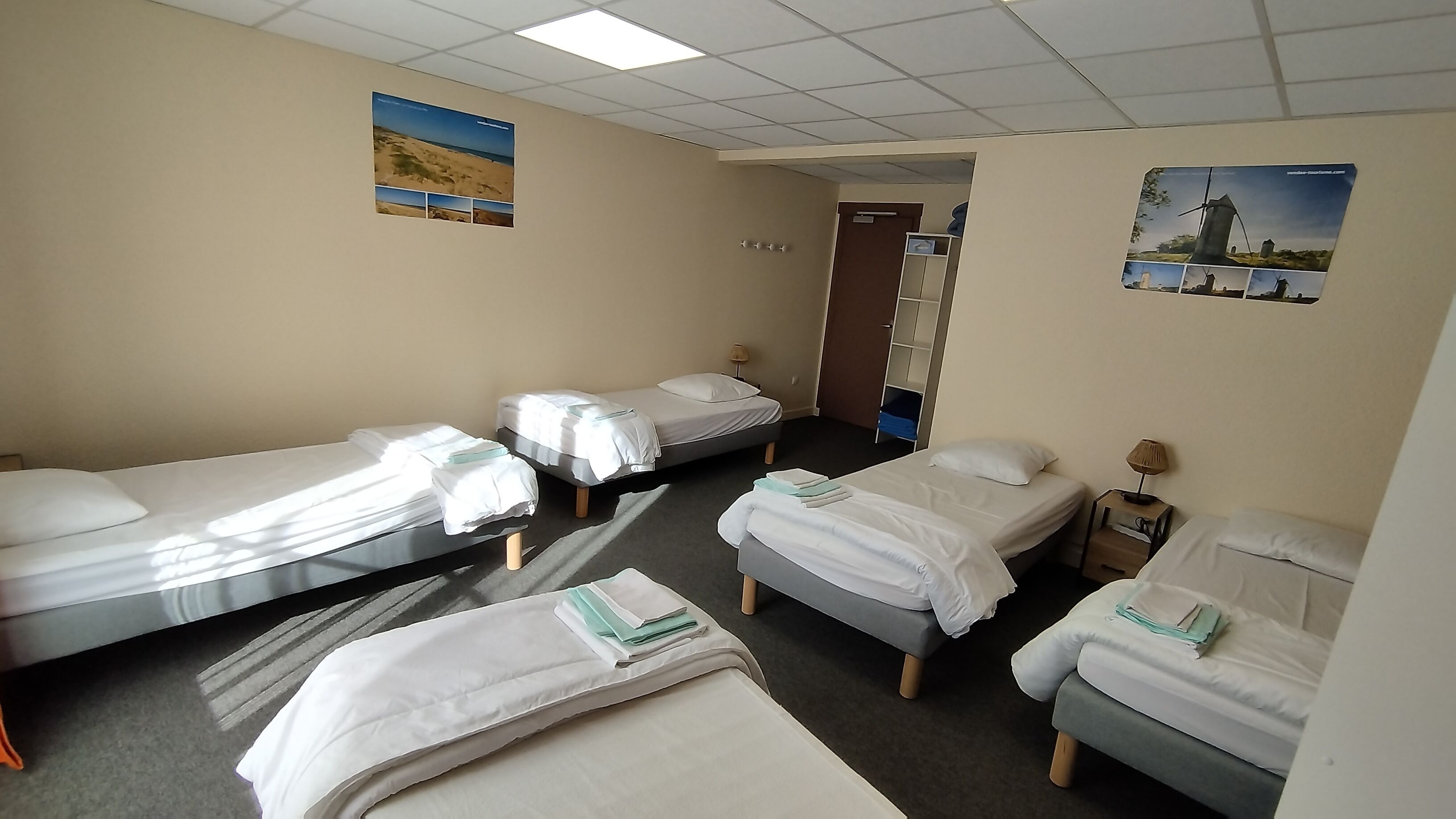 A hotel room with four single beds, a small desk with a lamp, and a door leading to a bathroom.
