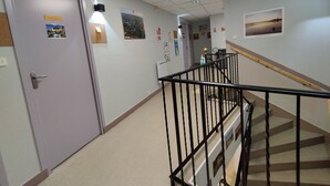 Un pasillo con una puerta que indica 'Chamberlain', una escalera con barandilla negra y una pared decorada con varios carteles y un cuadro enmarcado.