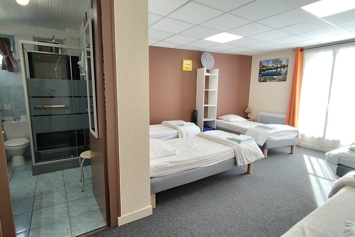 A hotel room with two beds, a bathroom, a window with curtains, and a wall-mounted fan.