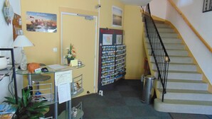 Zona de recepción con escritorio, planta, tablón de anuncios, escalera y pared decorada con cuadros.