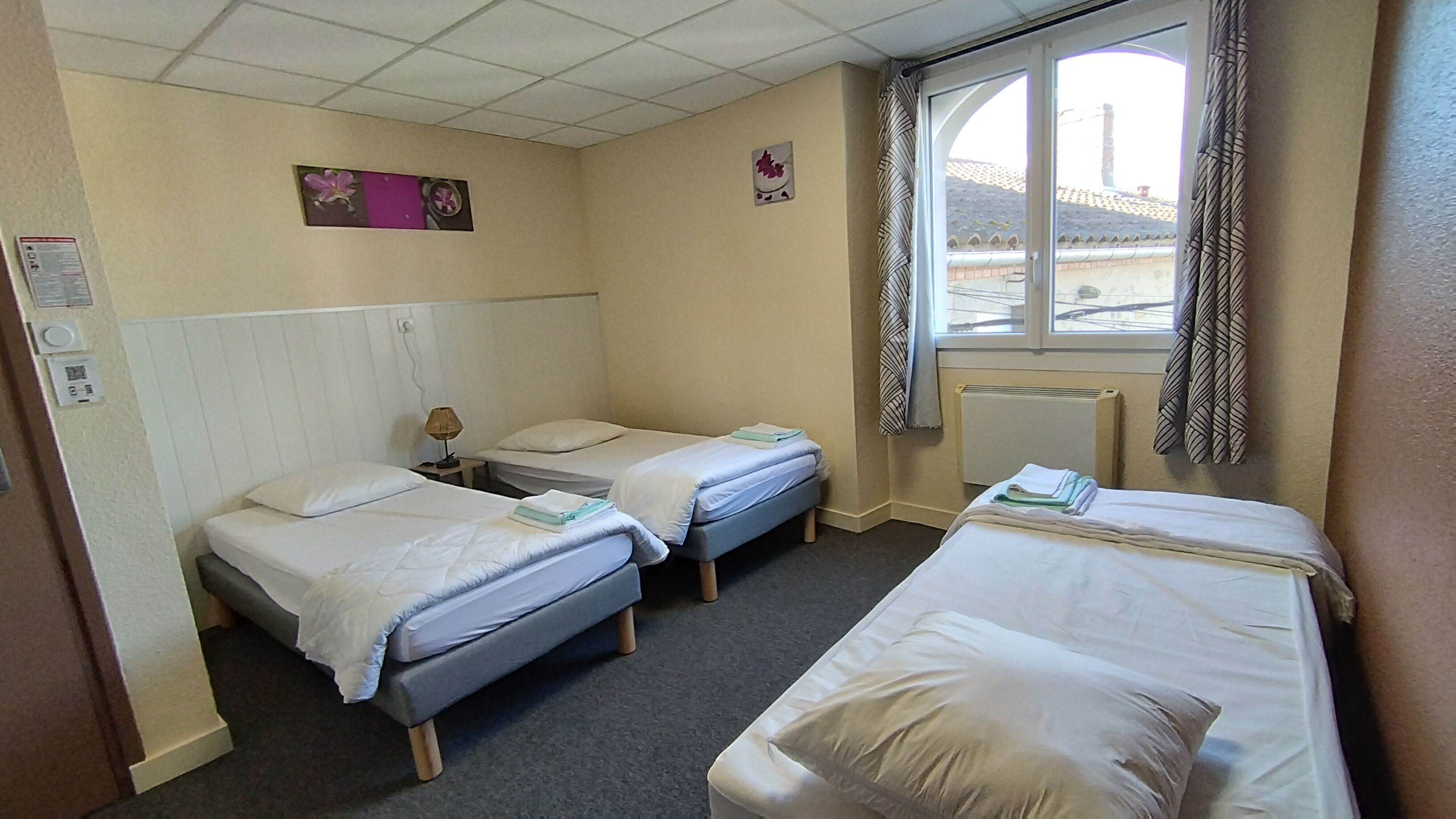 Een hotelkamer met twee eenpersoonsbedden, een klein tafeltje met een lamp, een radiator en een raam met gordijnen.