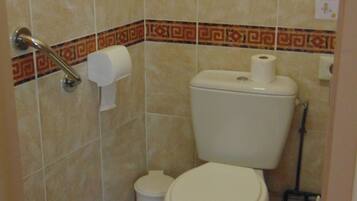 A bathroom with a toilet, a bidet, and a handrail.