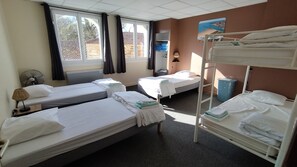 Habitación de hotel con cuatro camas, un ventilador, una ventana con cortinas, un televisor montado en la pared y vistas al exterior.