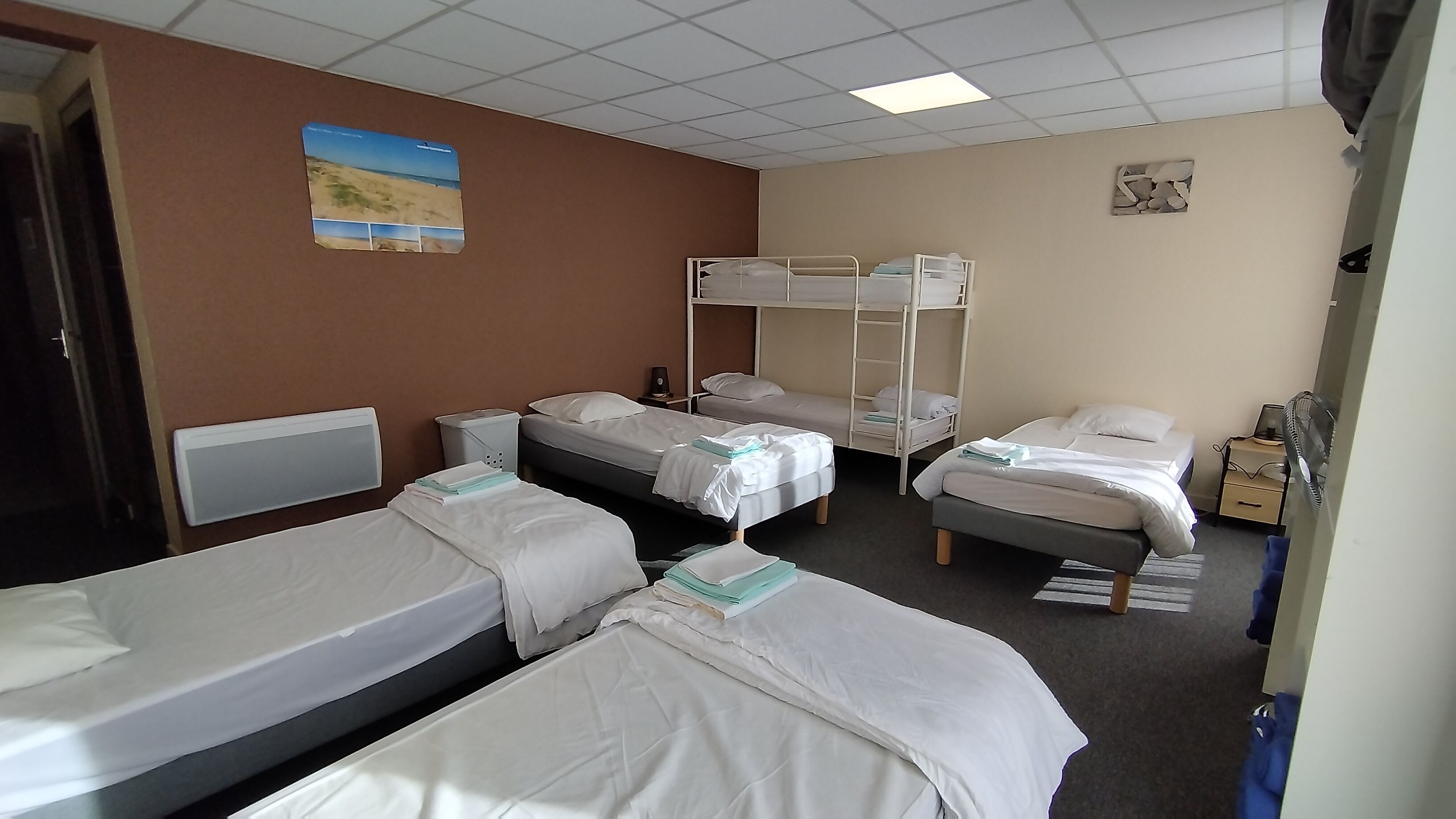 A hotel room with bunk beds, a bedside table, a lamp, and a wall-mounted picture.