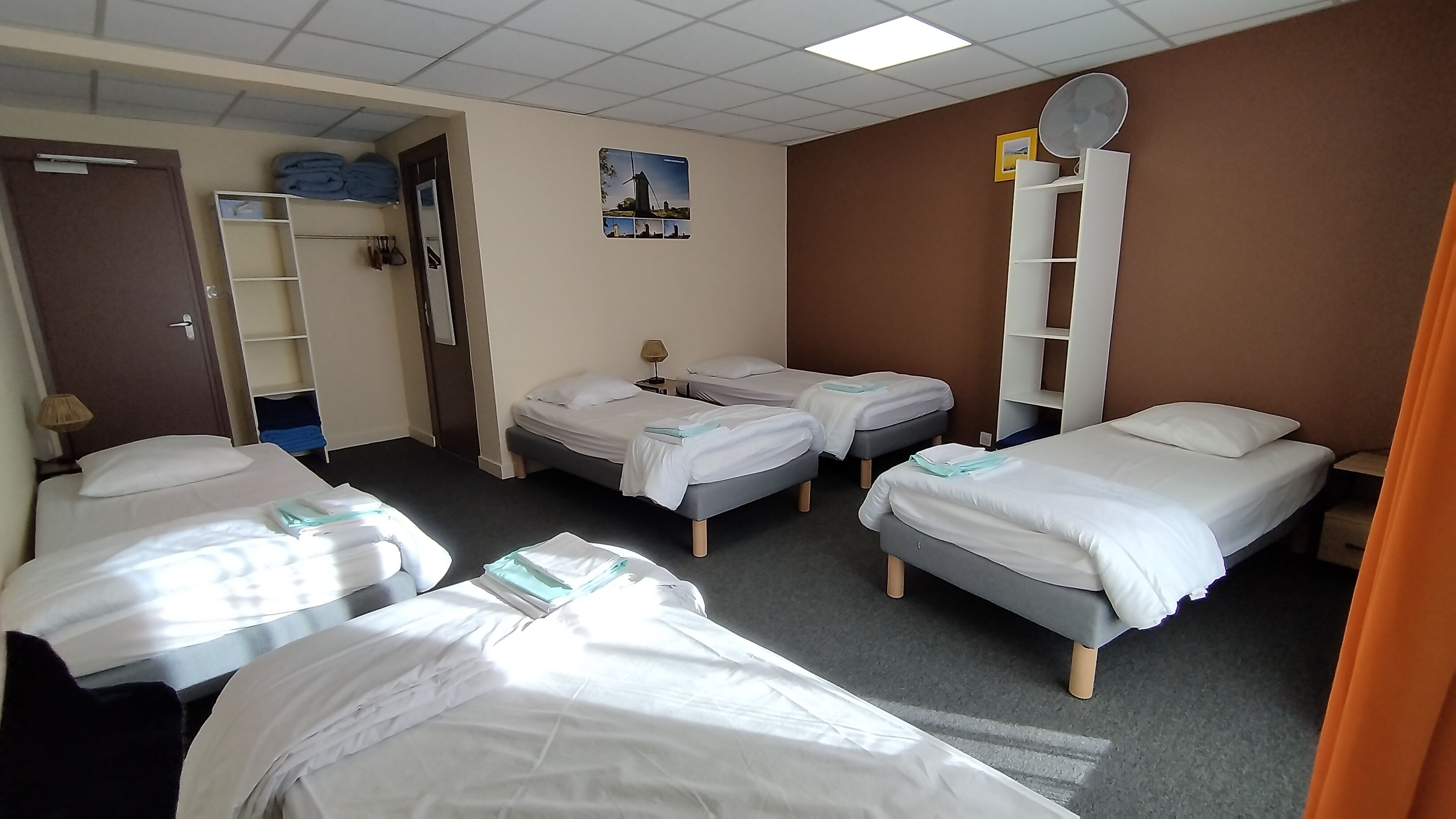 Una habitación de hotel con cuatro camas individuales, un armario, un espejo y un cartel en la pared.