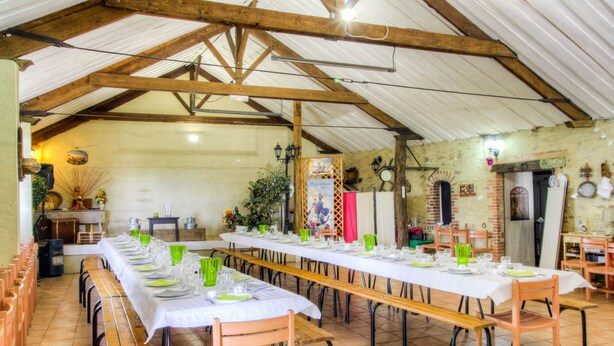 Una larga mesa de comedor dispuesta para una comida en un comedor rústico con vigas de madera y paredes de ladrillo.