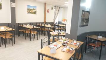 A dining area with multiple tables and chairs, a large window with a view, and a wall-mounted projector screen.