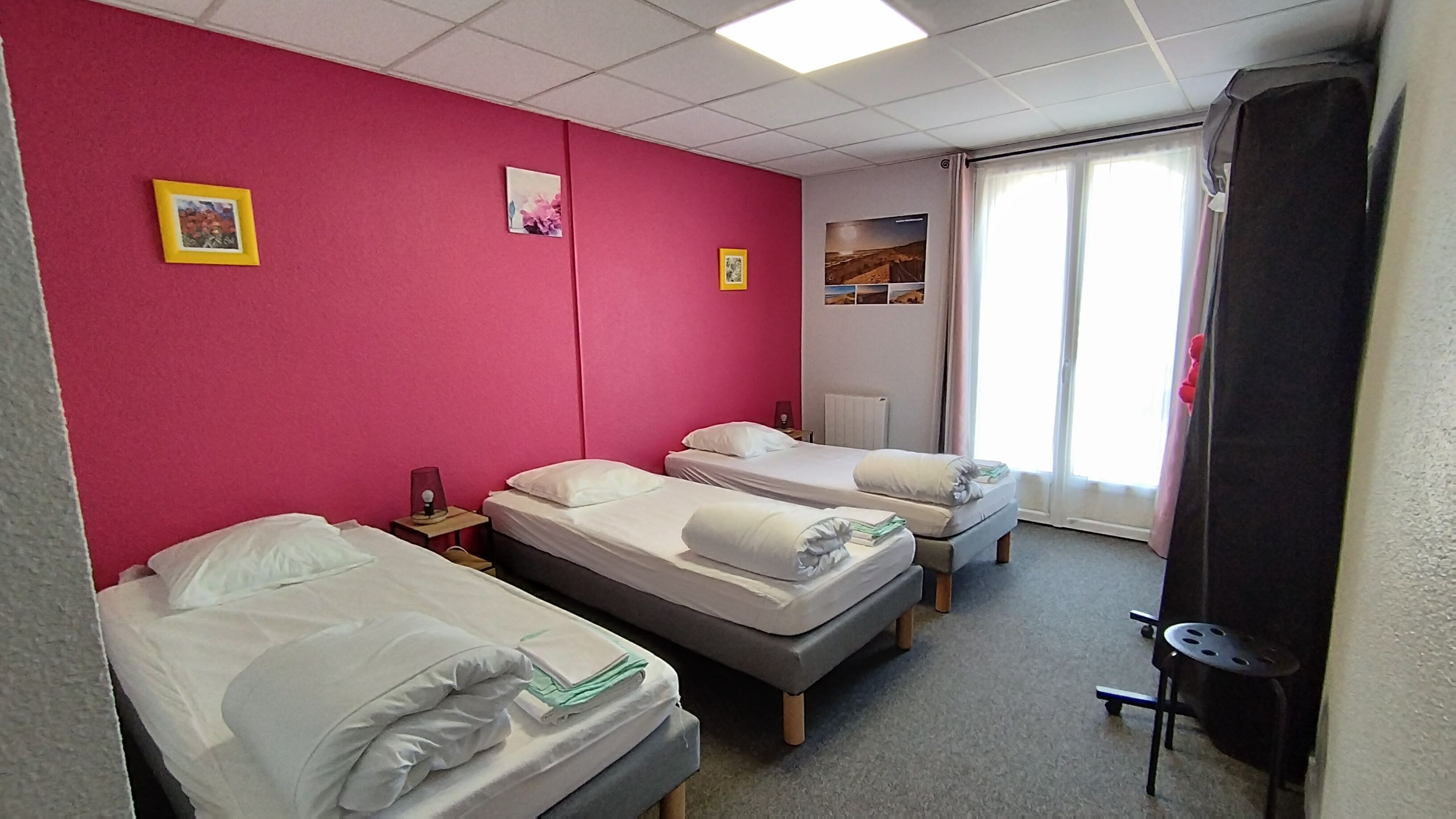 Ein Hotelzimmer mit drei Betten, einem Schreibtisch, einem Stuhl und einem Fenster mit Blick.