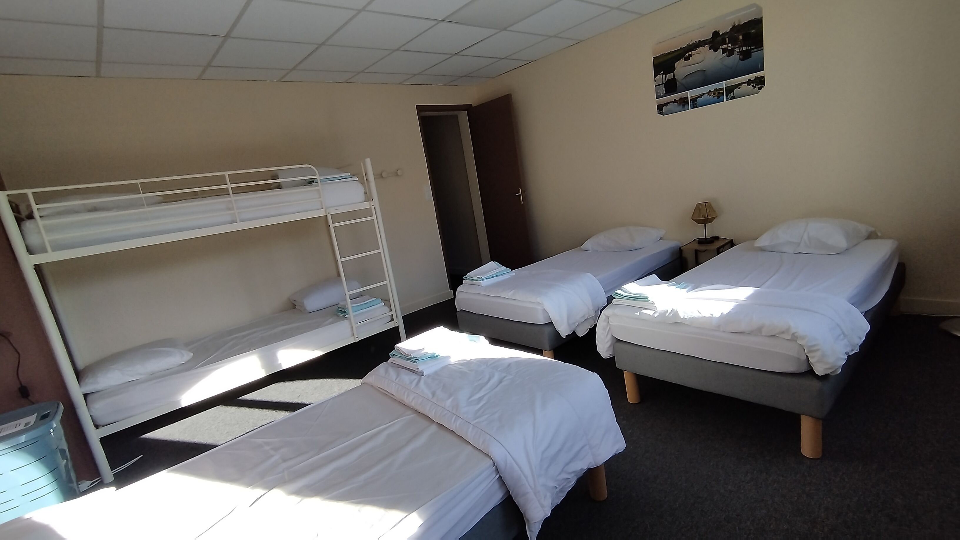 A room with bunk beds, two single beds, a nightstand with a lamp, and a door.