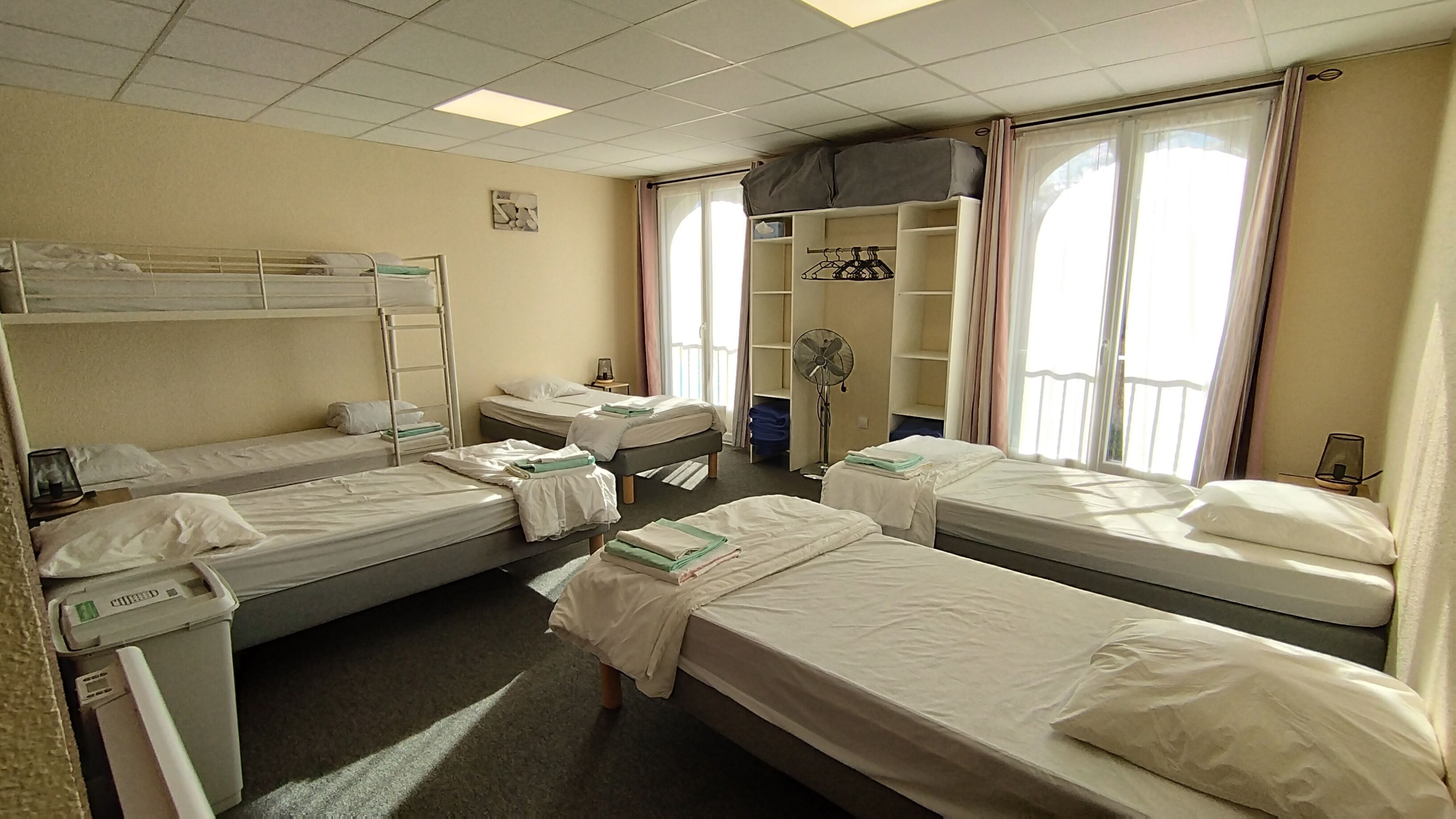 A hotel room with bunk beds, a fan, a wardrobe, and a window with curtains.
