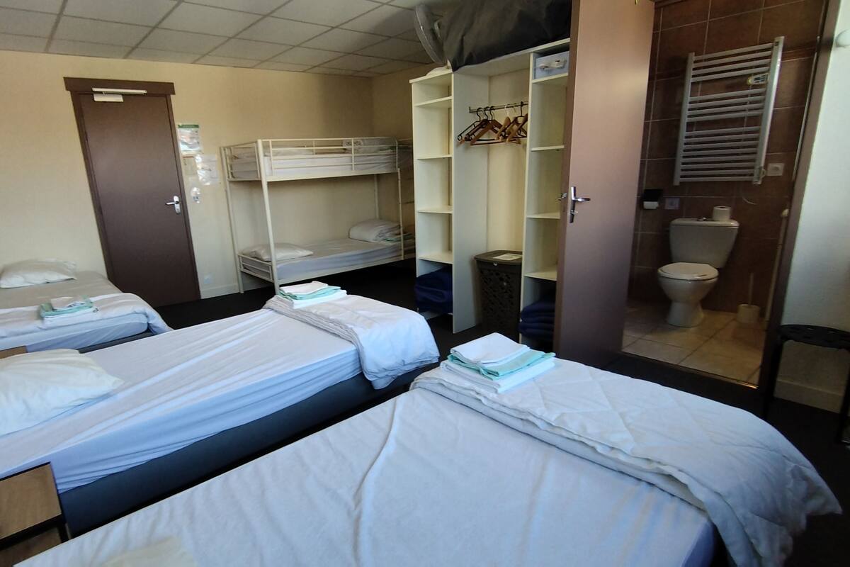 A hotel room with two single beds, a wardrobe, a bathroom with a toilet and shower, and a desk with a lamp.