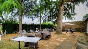 Un espacio al aire libre con patio, mesa y sillas, rodeado de árboles y un muro de piedra.